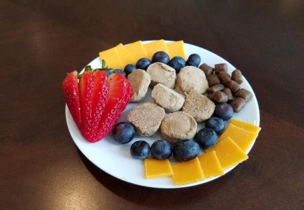 A plate of dog treats includes strawberry slices, blueberries, cheese, training treats, and a few freezes-dry dog treats.